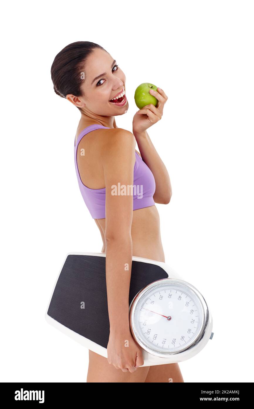 Changing her eating habits means weightloss. Studio shot of an attractive young woman dressed in gym clothes holding an apple and weight scale. Stock Photo