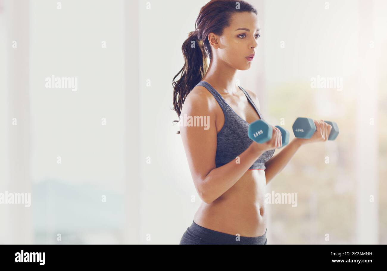 Building her biceps. Cropped shot of an attractive young woman working out with dumbbells in her home. Stock Photo