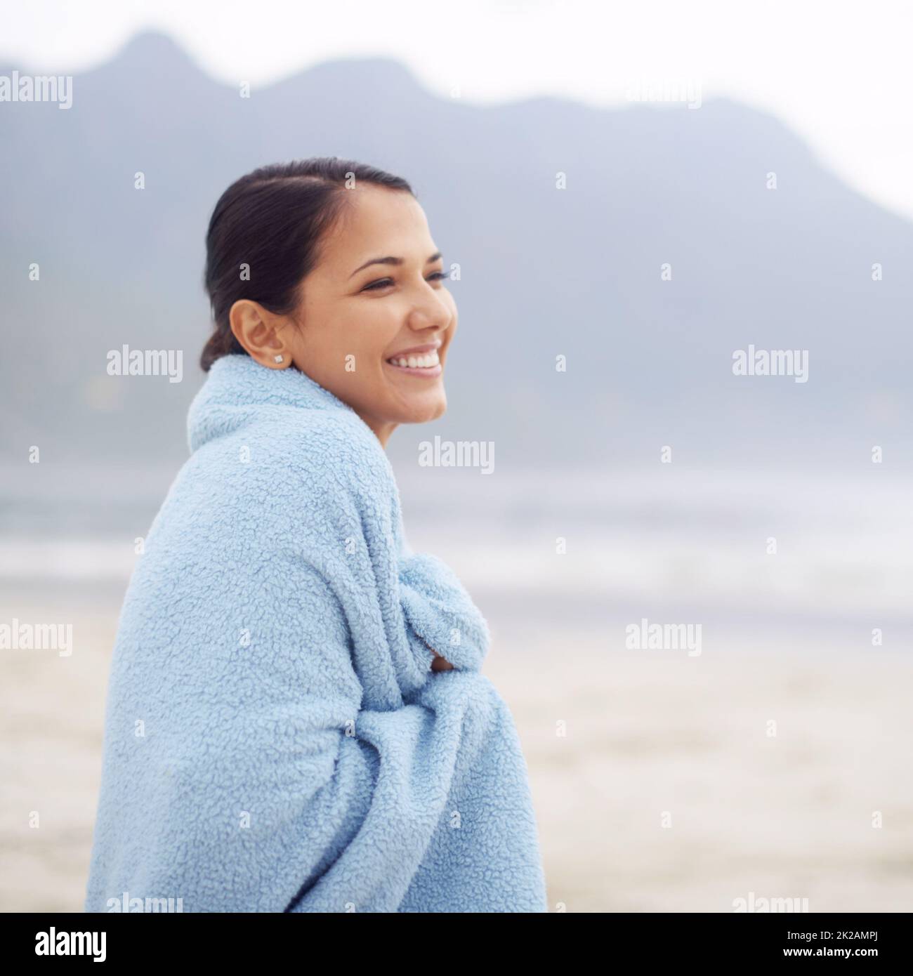 Its quiet out here on the beach. Shot of an attractive young woman sitting on the beach. Stock Photo