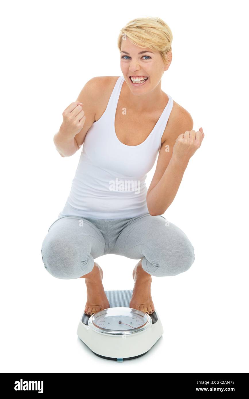 Yes Ive reached my target weight. A young blond woman standing on a scale with her arms raised in celebration. Stock Photo