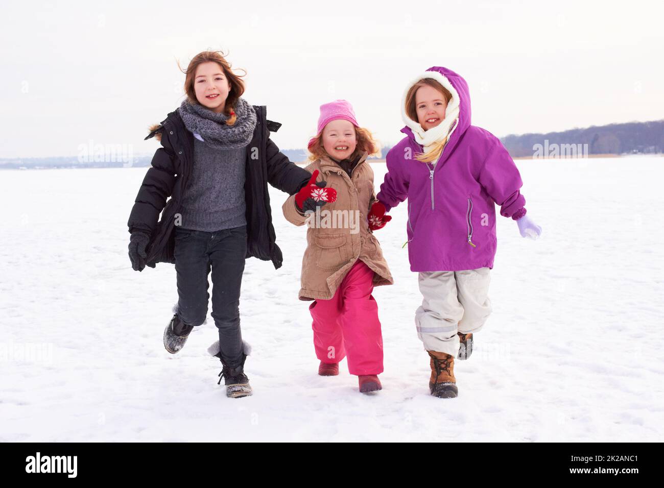 Lets go make snow angels. Three young sisters running outside in the snow. Stock Photo