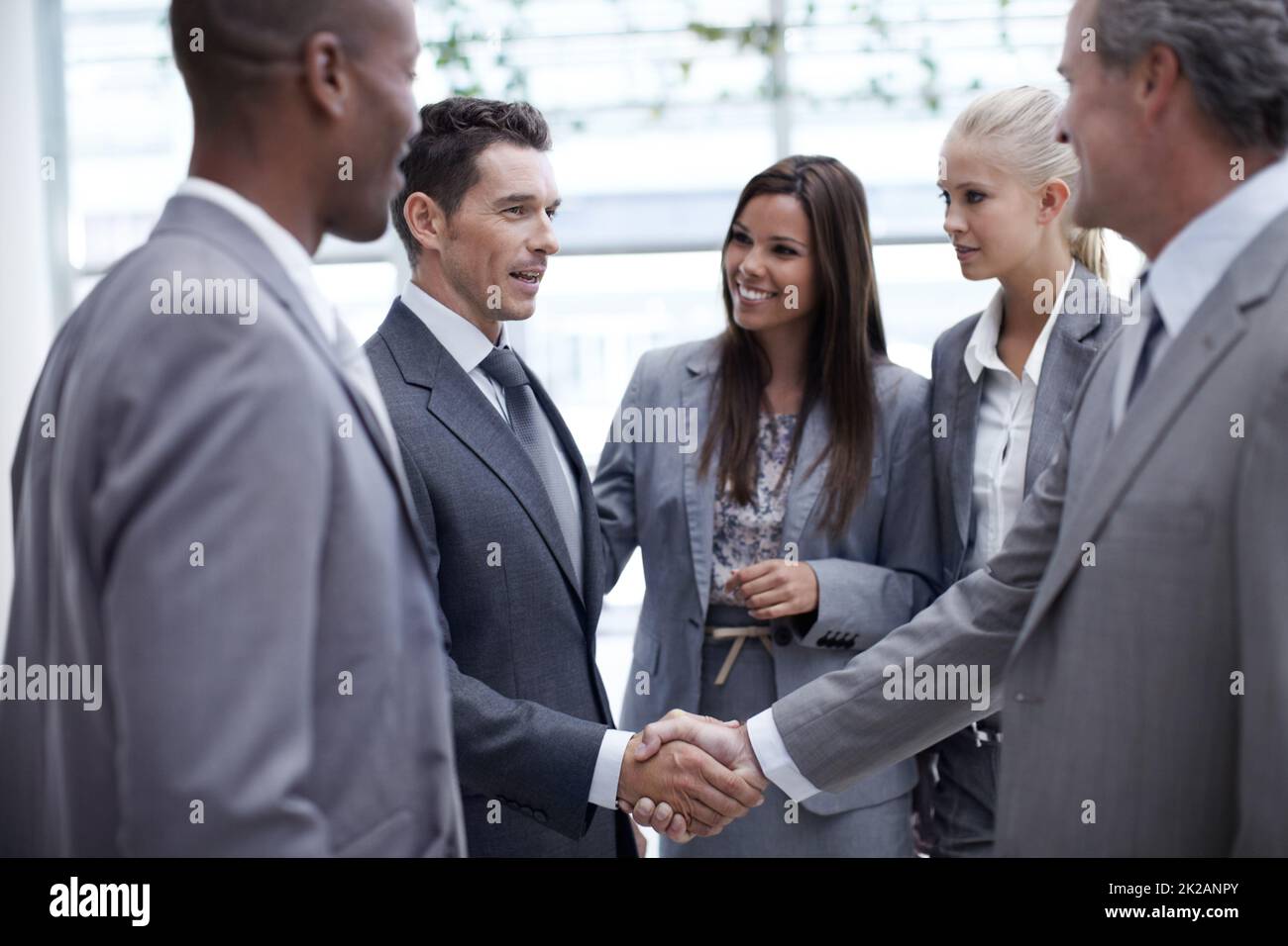 Climbing up the corporate ladder. A diverse group of businesspeople looking on as a coworker and their boss shake hands. Stock Photo