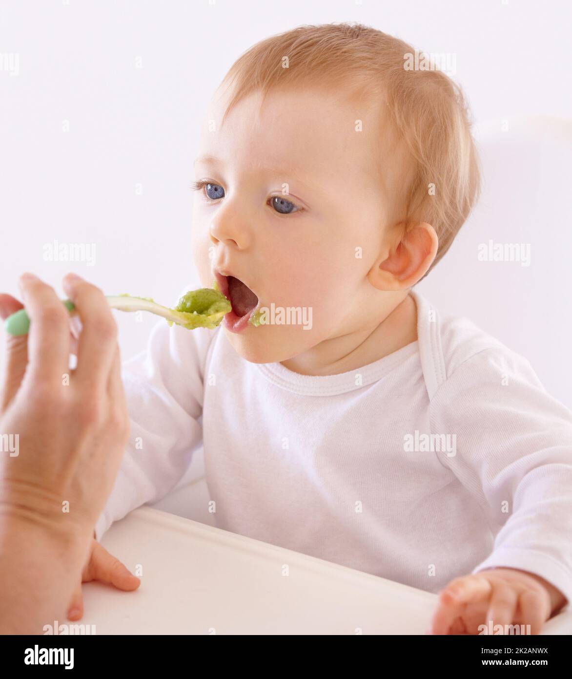 Hes got a good appetite. A cute baby accepting a spoonful of food by his mom. Stock Photo
