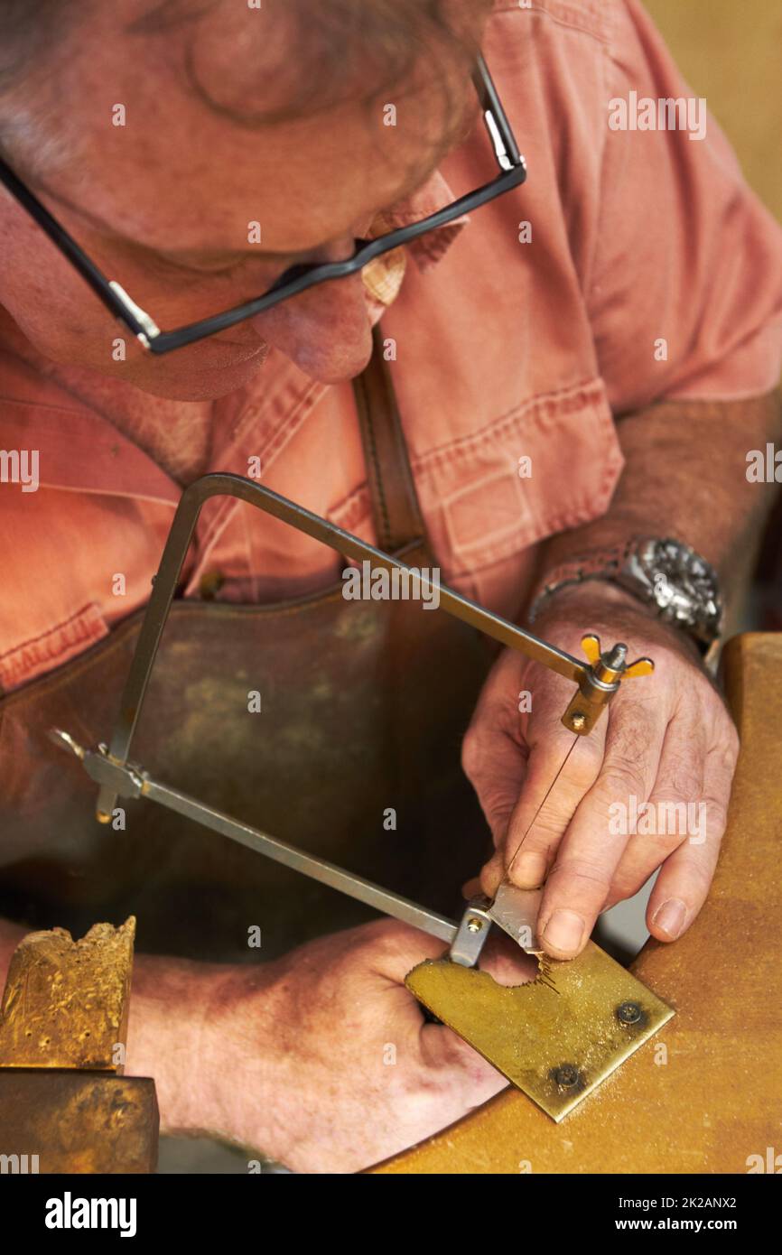 Carefully cutting out the shape - Jewelry manufacturing. Top view of a goldsmith about to saw into a piece of metal. Stock Photo