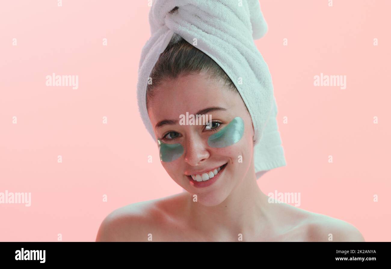 Always take care of your skin. Studio portrait of a young woman smiling with an eye treatment on her face against a pink background. Stock Photo