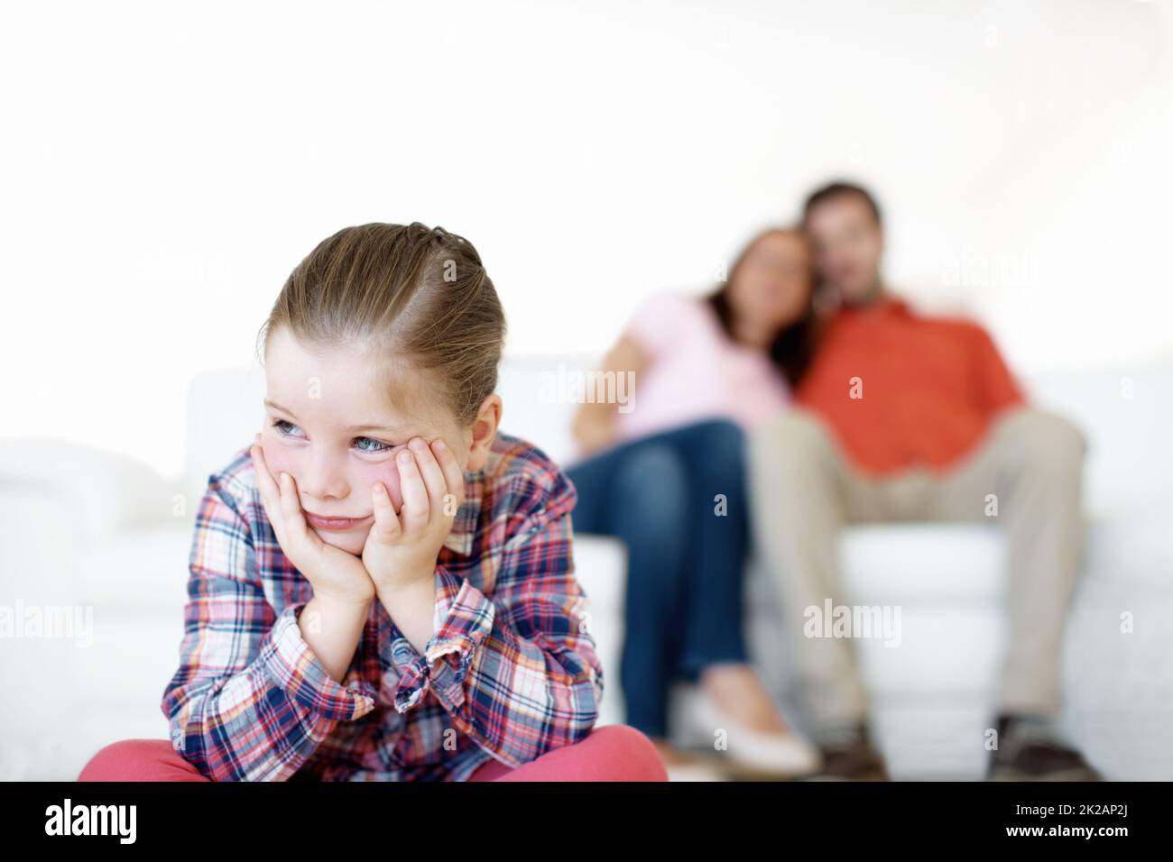 I hate timeout. A little girl sits and sulks while her parents in the background. Stock Photo