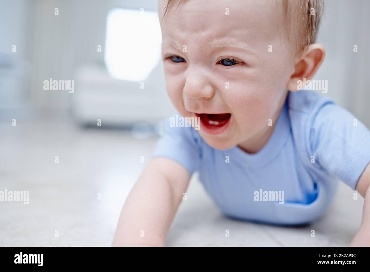 Teething is not fun. Closeup of a very unhappy baby boy lying on the floor. Stock Photo