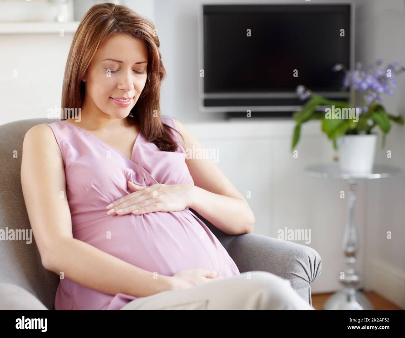 Not long now.... A glowing pregnant woman looking at her swelling baby bump. Stock Photo