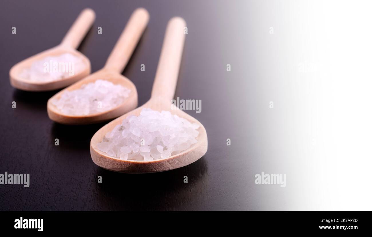 Bath salt in three wooden spoons on a dark polished desk in backlight Stock Photo
