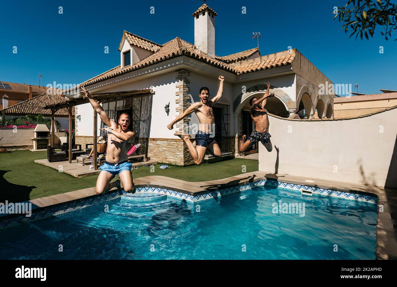 3 friends jumping into a pool doing a pirouette Stock Photo