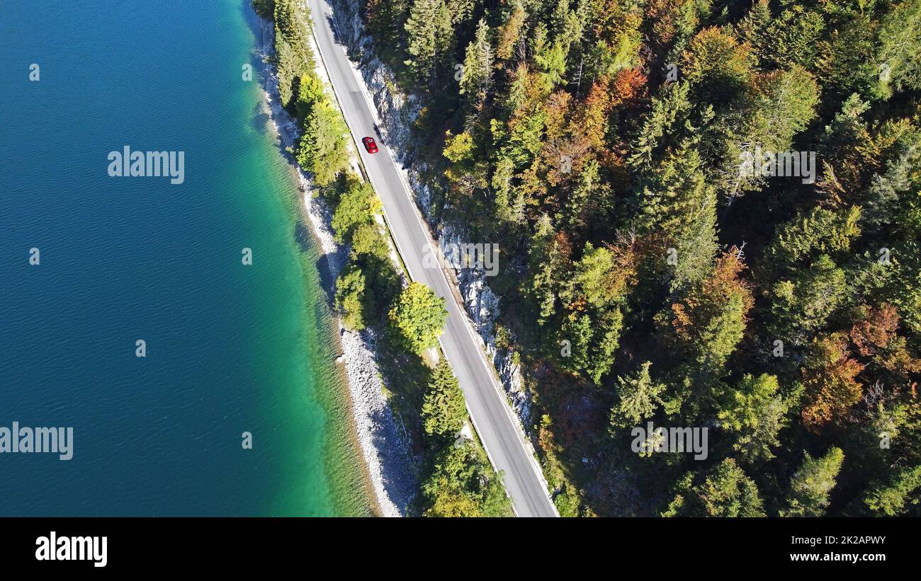 Aerial drone shot of red car road between lake and autumn forest Stock Photo