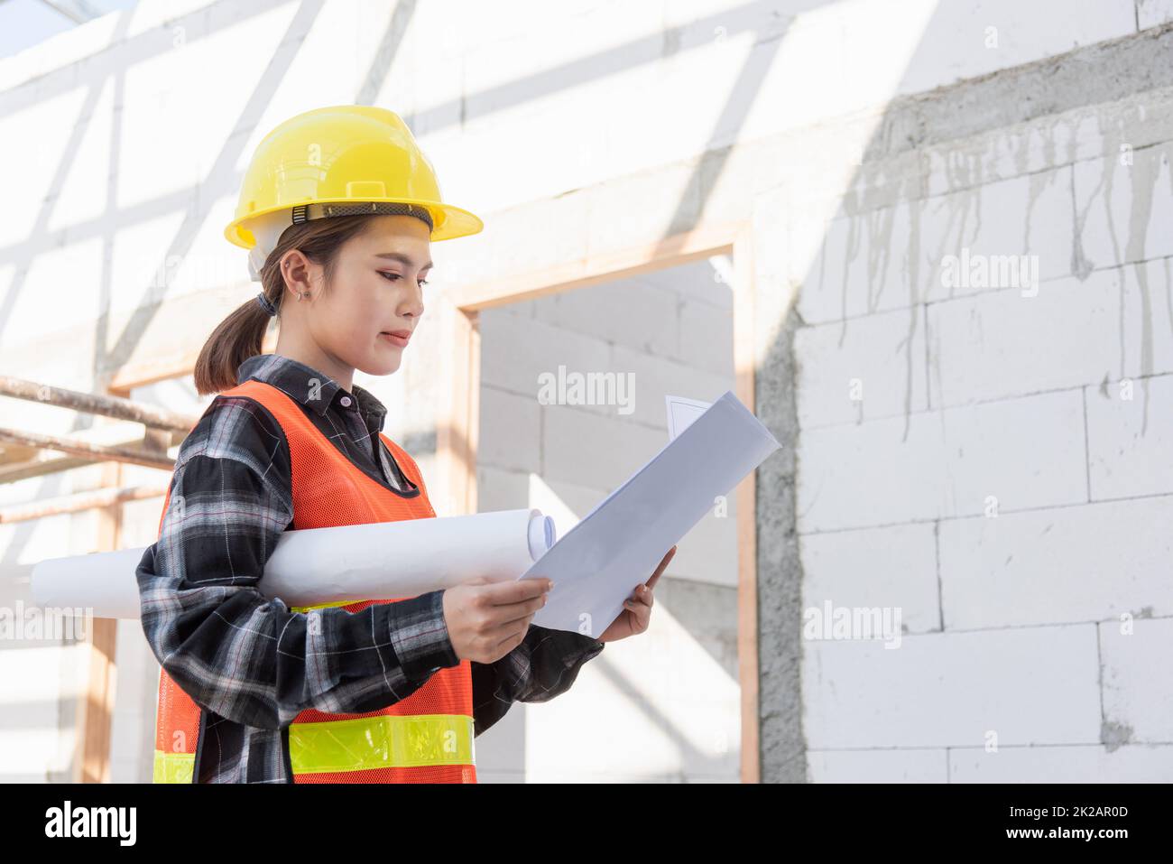 Asian engineer architect worker woman holding blueprint infrastructure progress at construction site Stock Photo