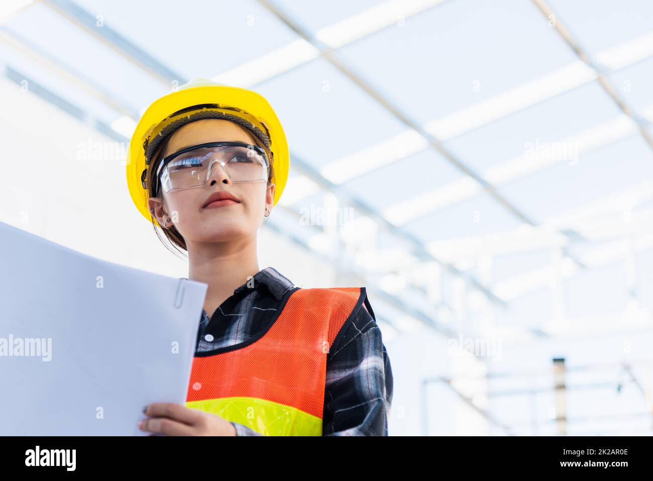 Asian engineer architect worker woman holding blueprint infrastructure progress at construction site Stock Photo