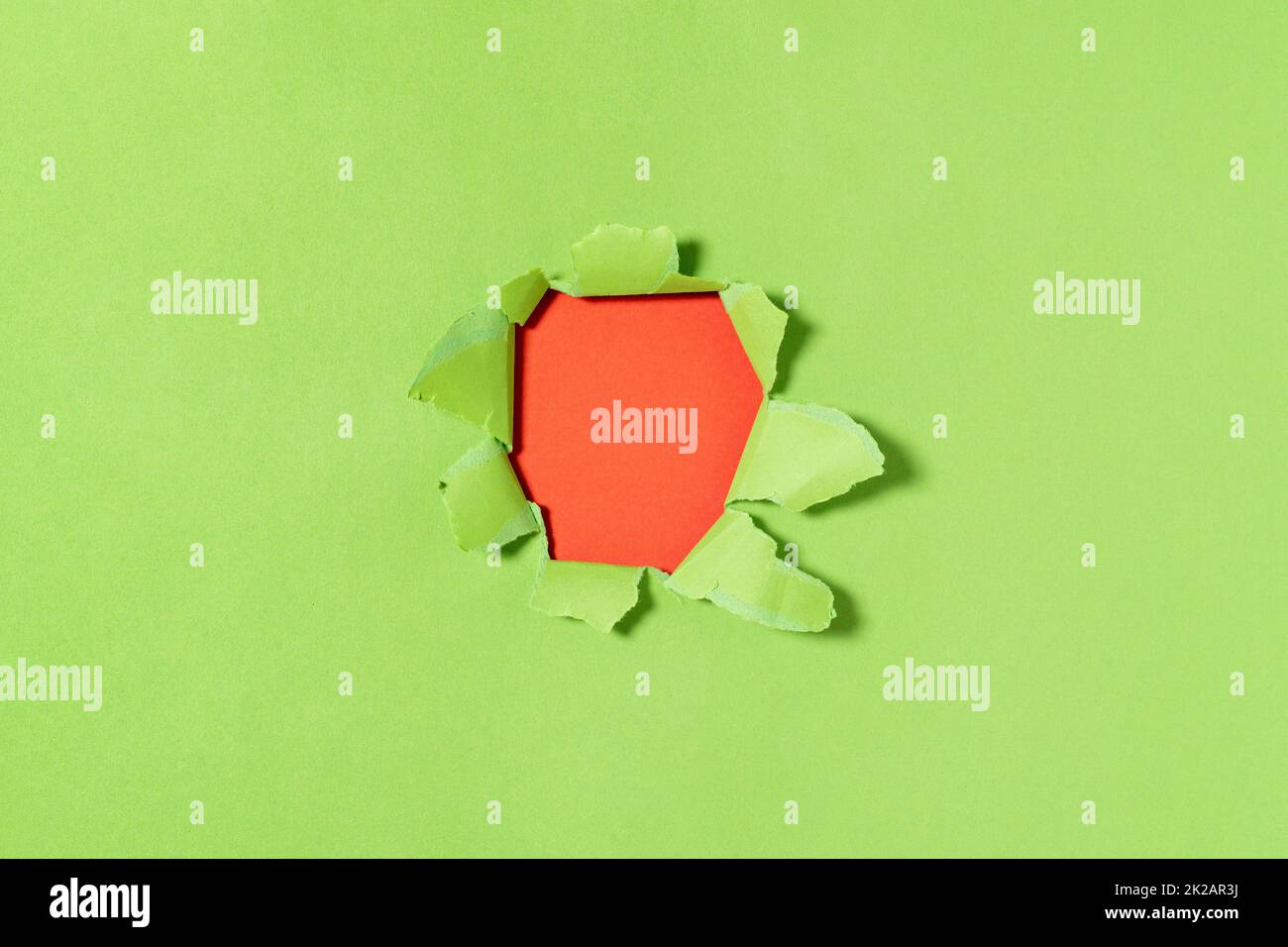 A hole in green paper with torn edges and a red  background inside Stock Photo