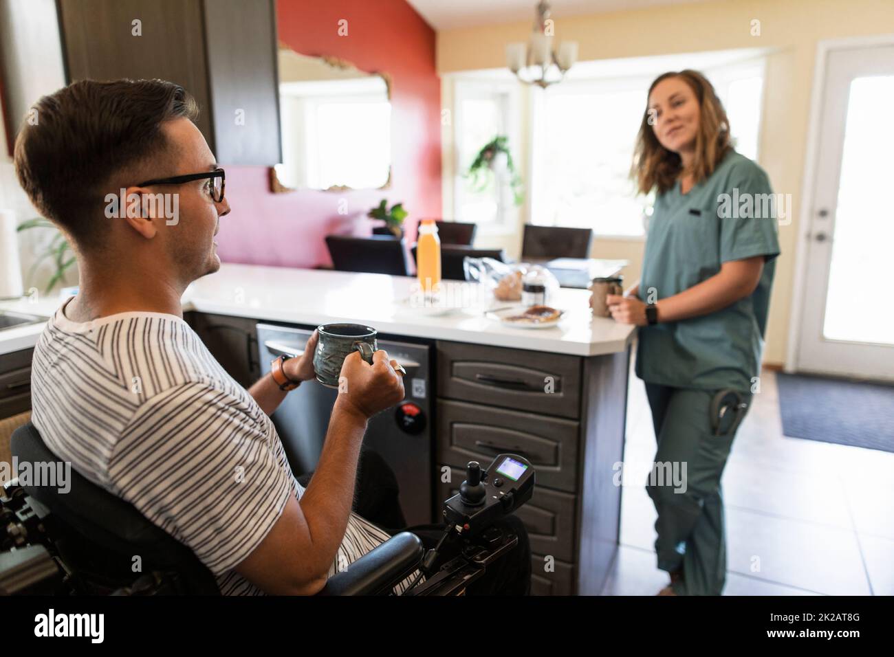 Quadriplegic man and medic girlfriend in scrubs having breakfast Stock