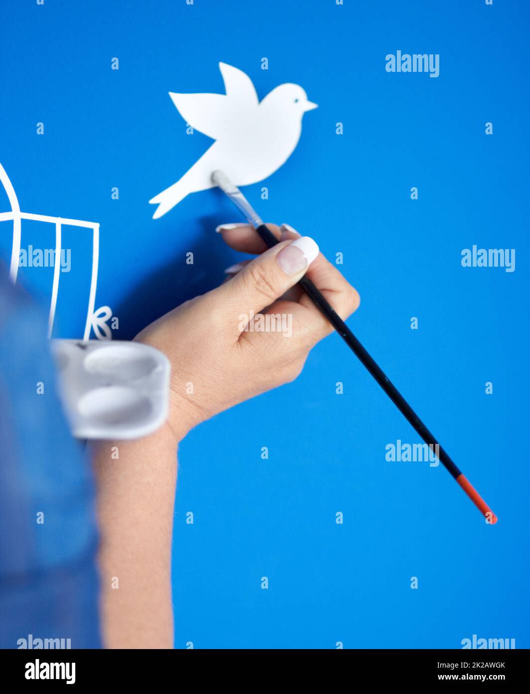 Creativity in flight. Closeup of a female artist painting a bird on a blue background. Stock Photo