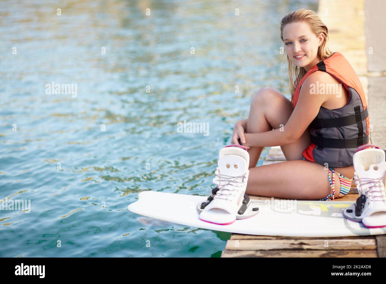 Portrait of a pretty young girl sitting on a jetty next to a wakeboard. Portrait of a pretty young girl sitting on a jetty next to a wakeboard. Stock Photo