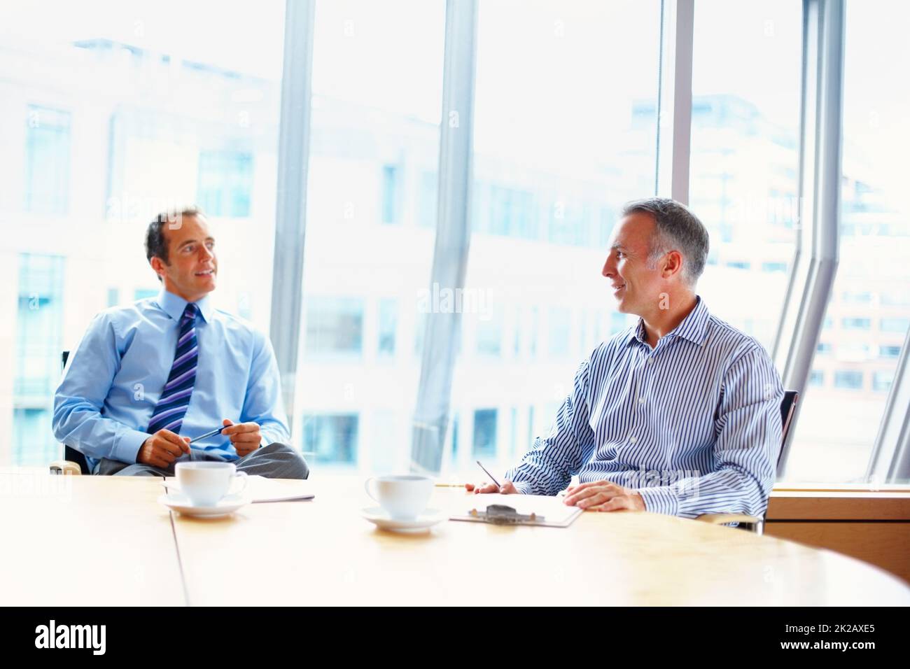 Executives in casual meeting over coffee. Two business men having casual meeting indoors at table. Stock Photo