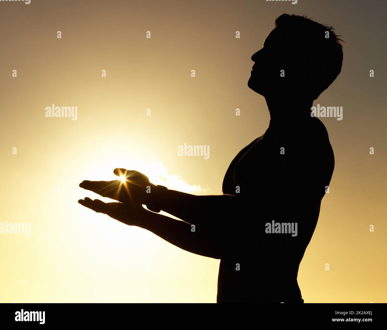 Salutation to the sun. A silhouette of a man standing calmly with his hands raised. Stock Photo