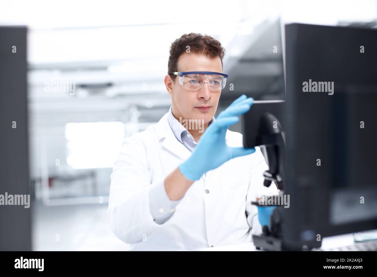 Making adjustments. A scientist looking intently at a microscope while wearing safety glasses. Stock Photo
