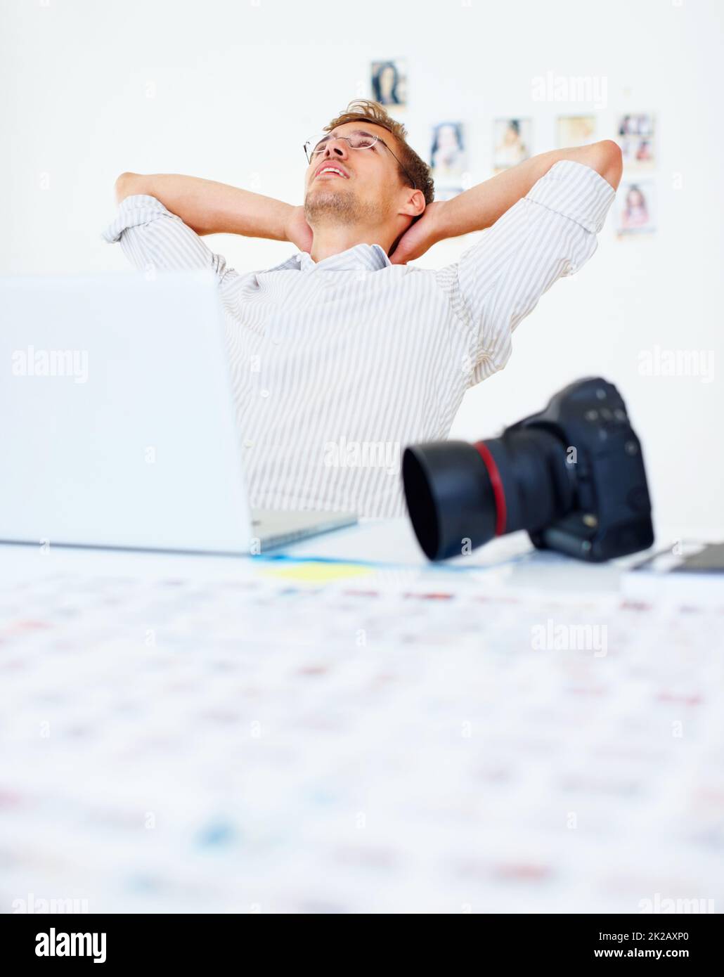 Photographer relaxing. Photographer using laptop and relaxing with hands behind head. Stock Photo