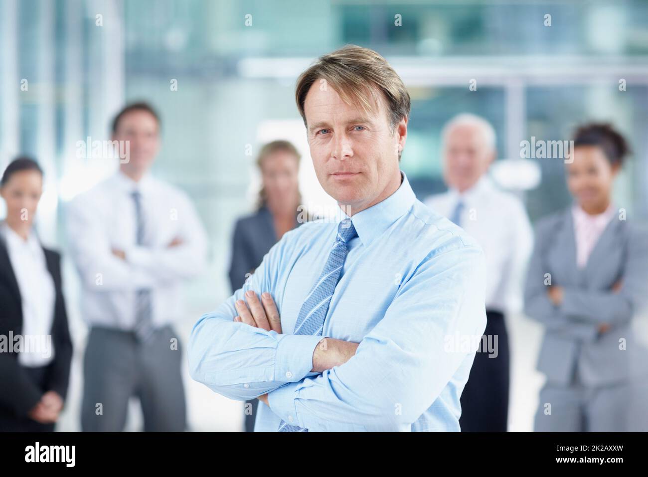 Hes worked hard for his success. Confident mature business executive standing with his team behind him - portrait. Stock Photo