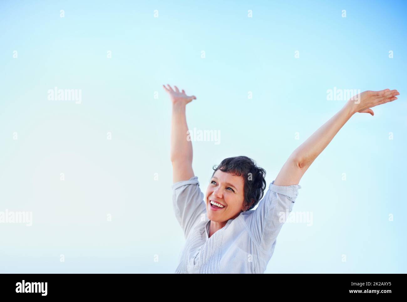 Pure joy. Happy mature woman enjoying freedom against blue sky with arms raised. Stock Photo