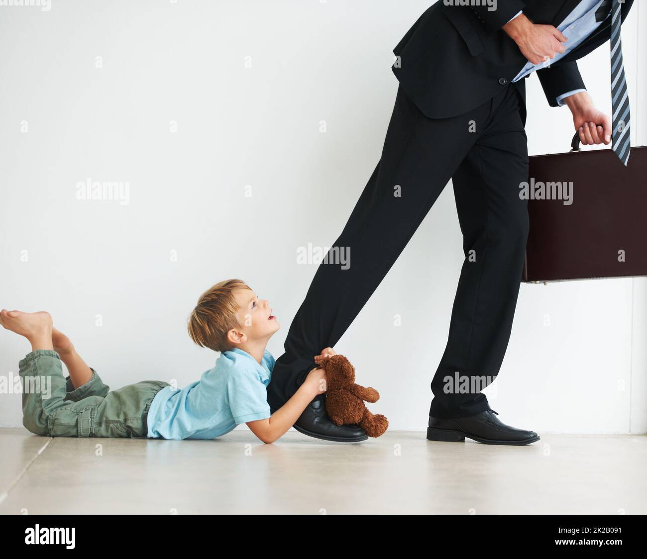 Stay at home with me daddy. A young boy holding onto his dads leg to try and stop him from leaving to work. Stock Photo