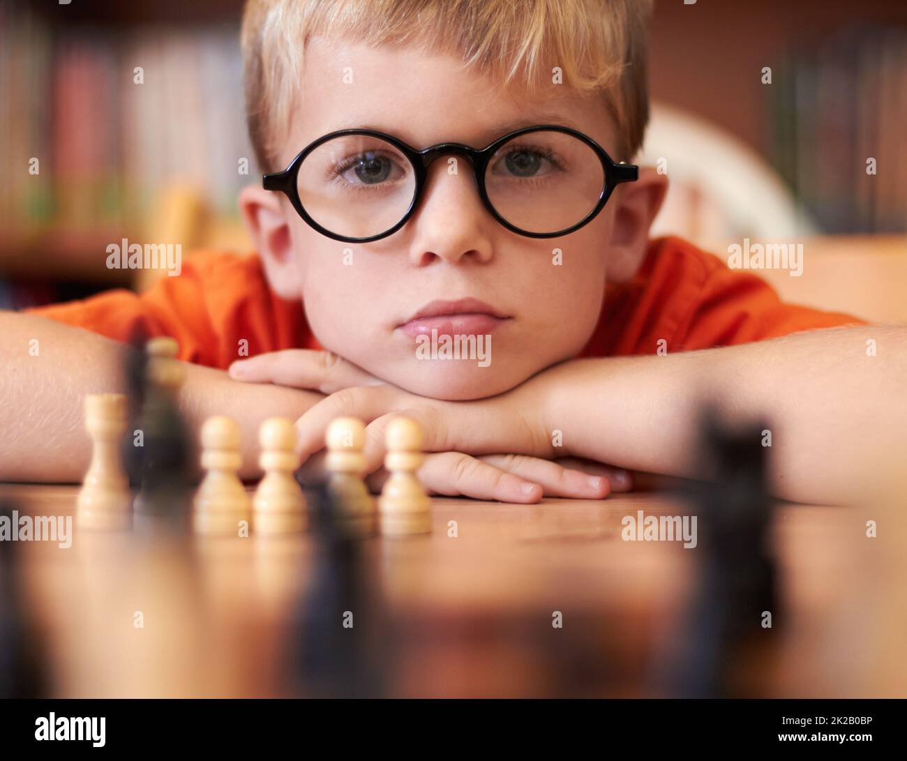 Pondering his next move. Young boy wearing spectacles and playing chess. Stock Photo
