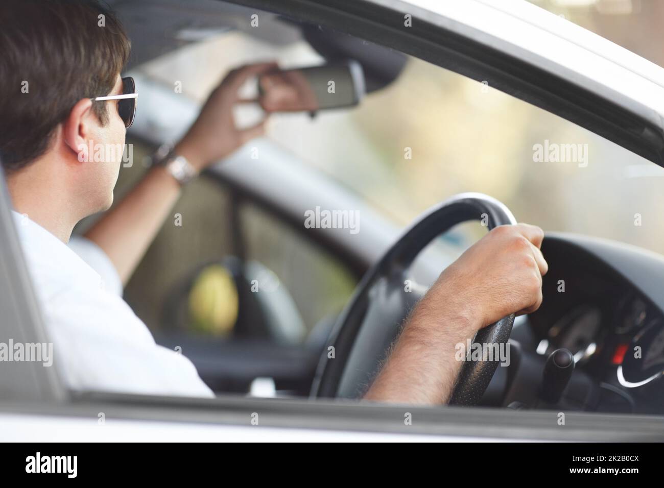 Seeing the road behind him. A man adjusting his rear view mirror while