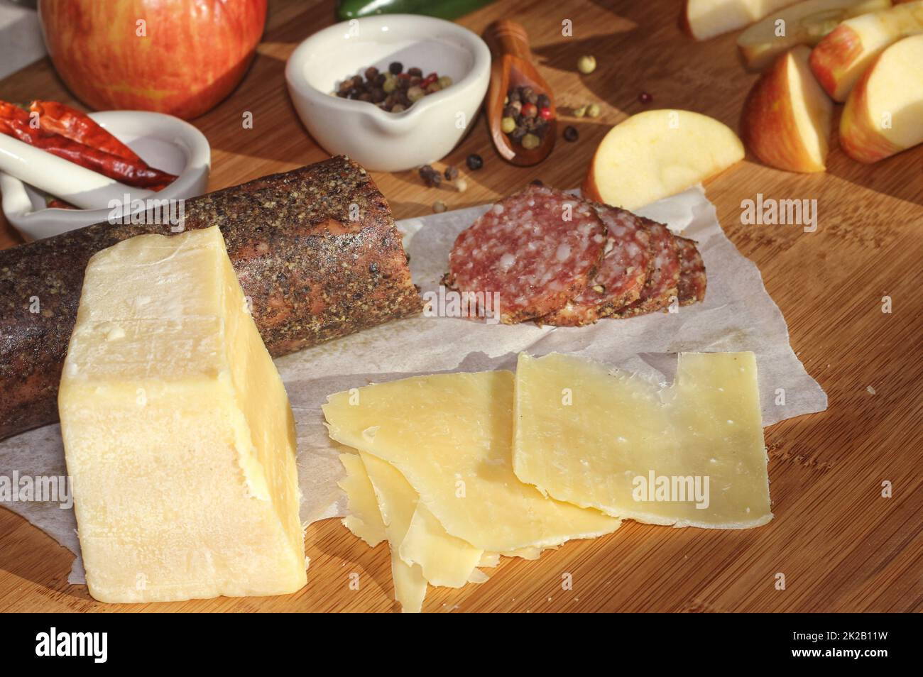 Peppercorn Salami on Tray With English and Irish Cheese, Sliced Apples and Spices in Rustic Kitchen Stock Photo