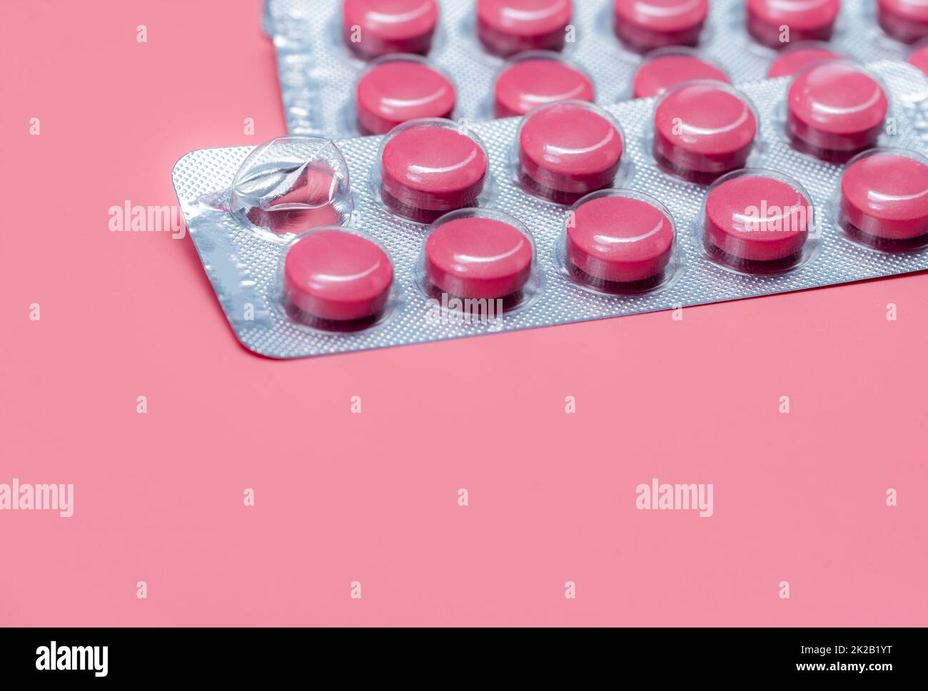 Take pill concept. Pink tablets pills in blister pack on pink background. Prescription drug. Pharmaceutical industry. Pill reminder or medication reminder background. Vitamin, mineral, and supplement. Stock Photo