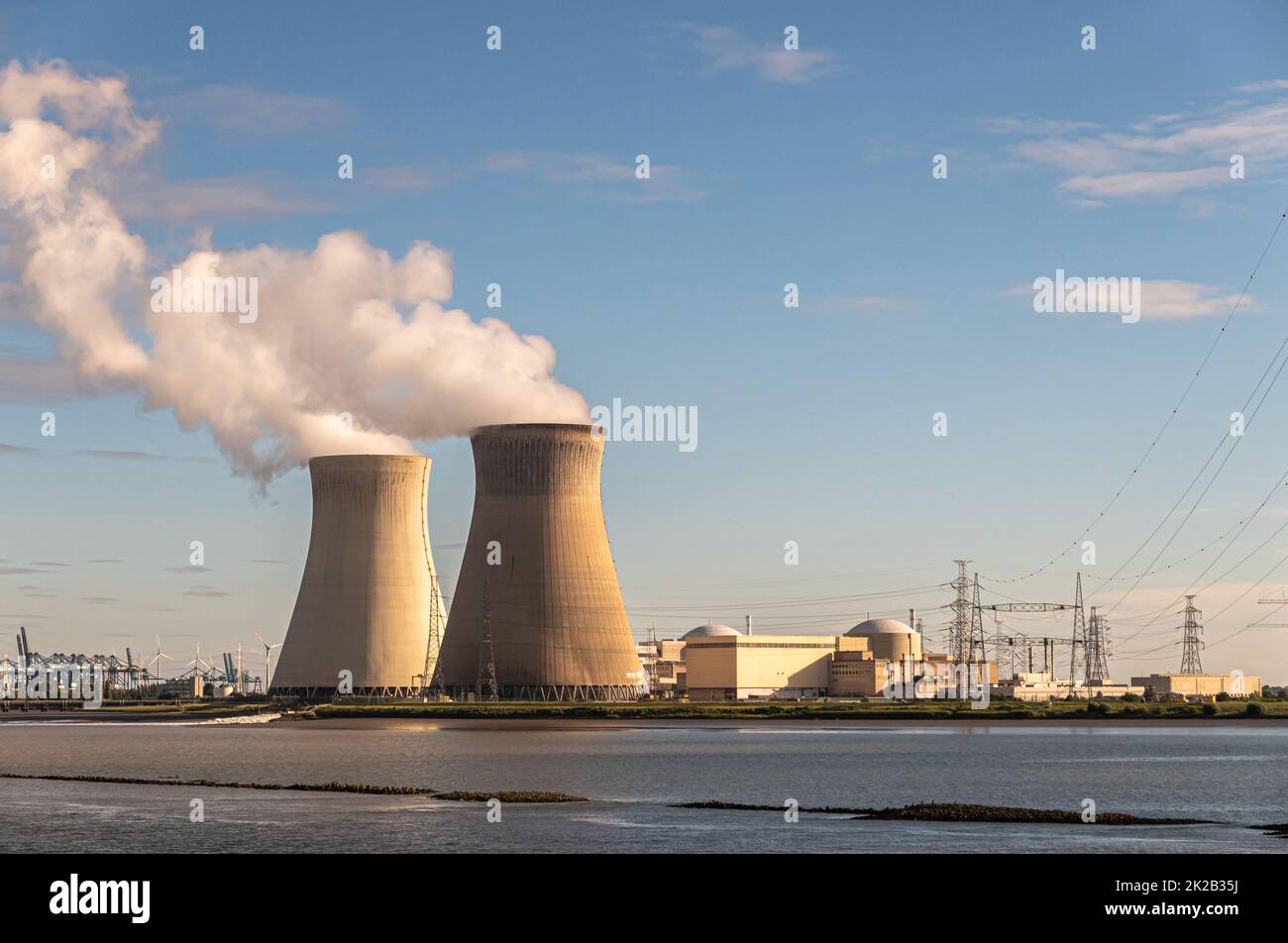 Antwerpen, Flanders, Belgium - July 10, 2022: Sunset on Cooling towers and Doel Nuclear Power plant under blue sky and Scheldt river up front. Contain Stock Photo