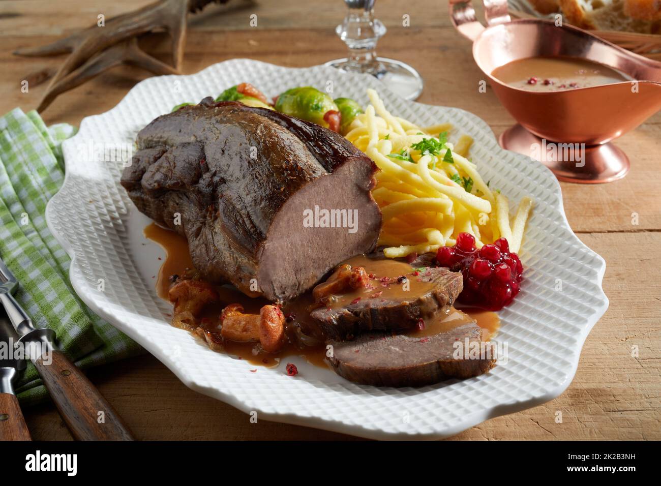 From above sliced delicious deer venison served with cranberry sauce on plate near potato fries and Brussels sprouts on wooden table during dinner Stock Photo