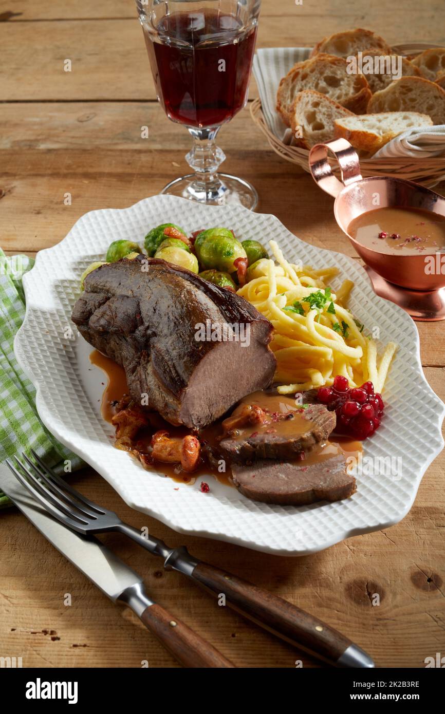 From above venison and vegetables served on plate near red wine and bread with sauce on lumber table Stock Photo