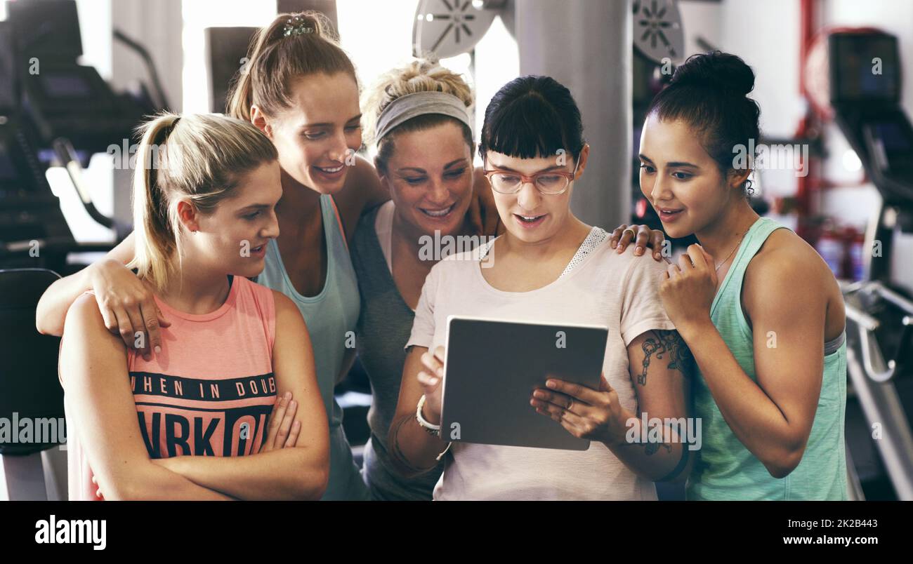 Showing them her fitness app. Cropped shot of a group of young women looking at a digital tablet in the gym. Stock Photo