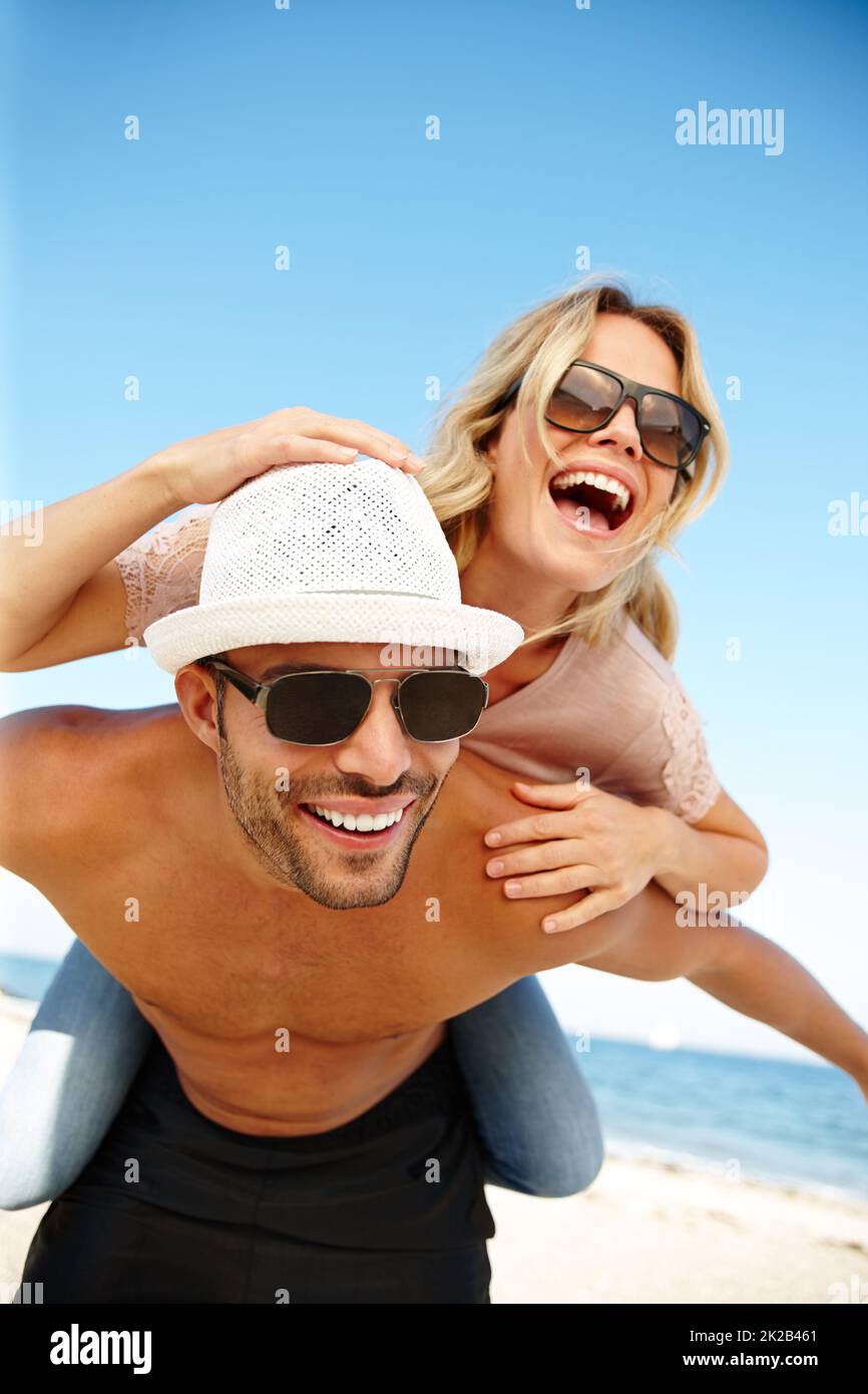 Fun-filled vacay days. Shot of a smiling young man giving his laughing girlfriend a piggyback on a sunny beach. Stock Photo