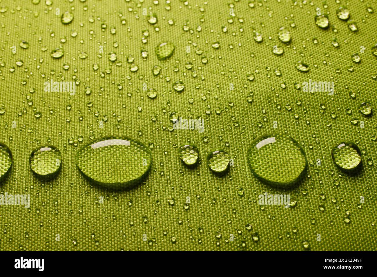 Overhead view of green fabric with closeup drops of water on wet textile coated with waterproof membrane in light room Stock Photo