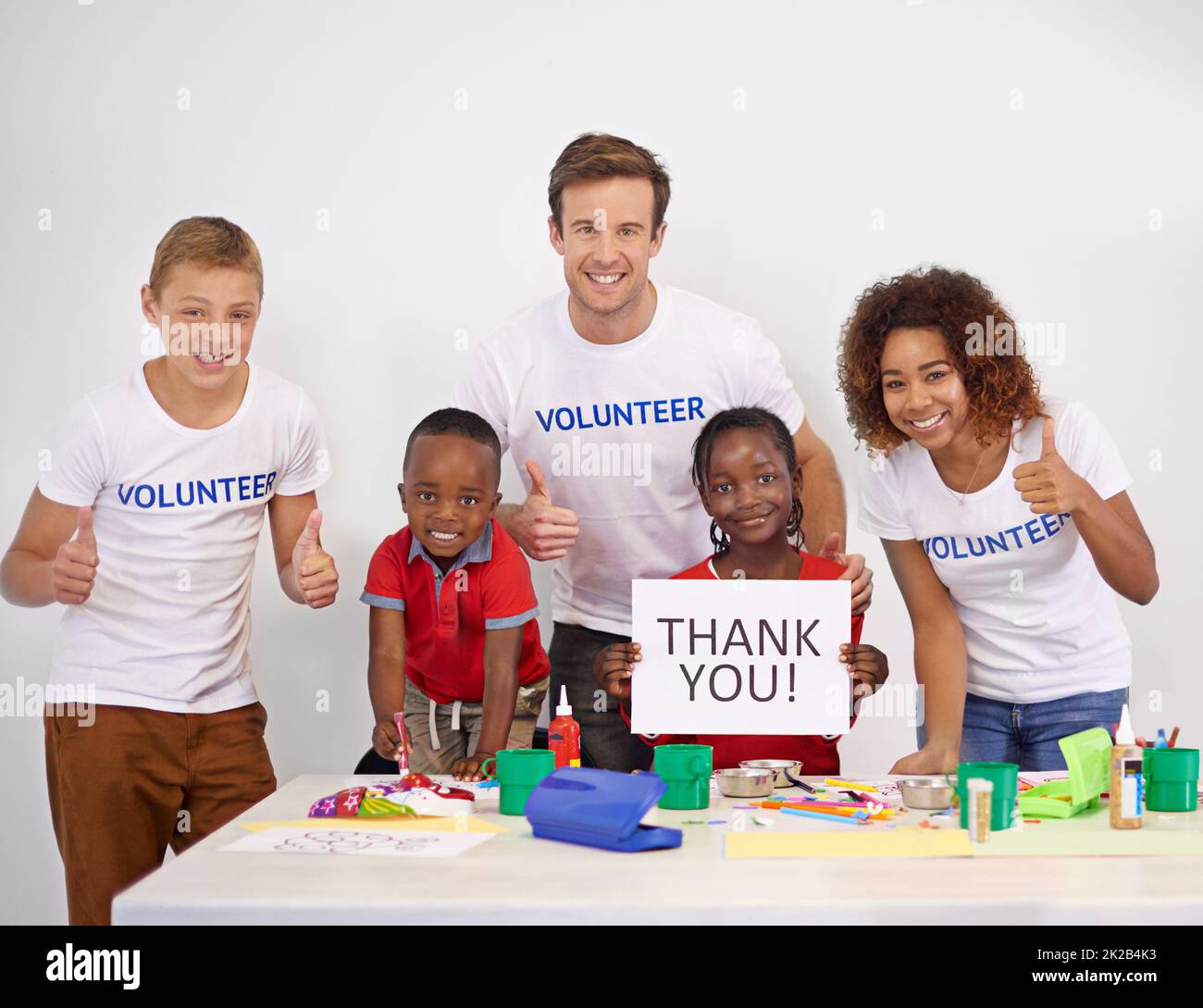 Every child needs someone to look up to. Portrait of a volunteer holding up a thank you sign while working with little children. Stock Photo