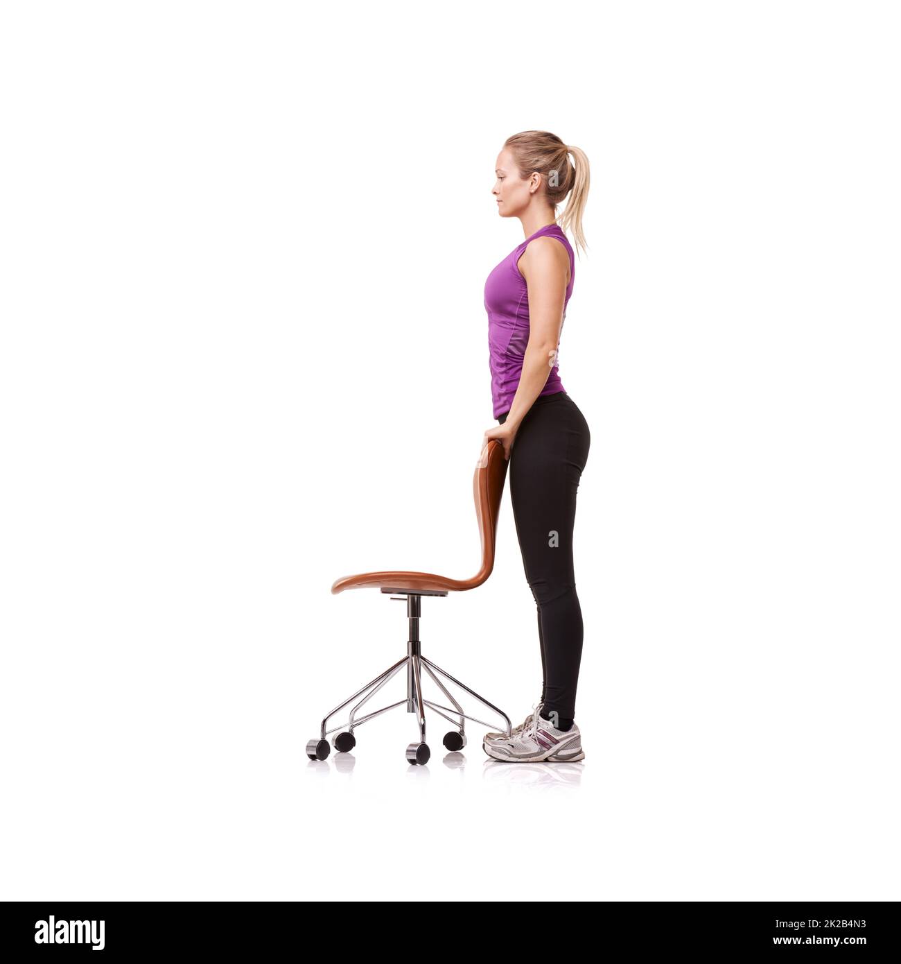 Standing strong. A beautiful young woman wearing gym clothes and standing while using a chair for support against a white background. Stock Photo