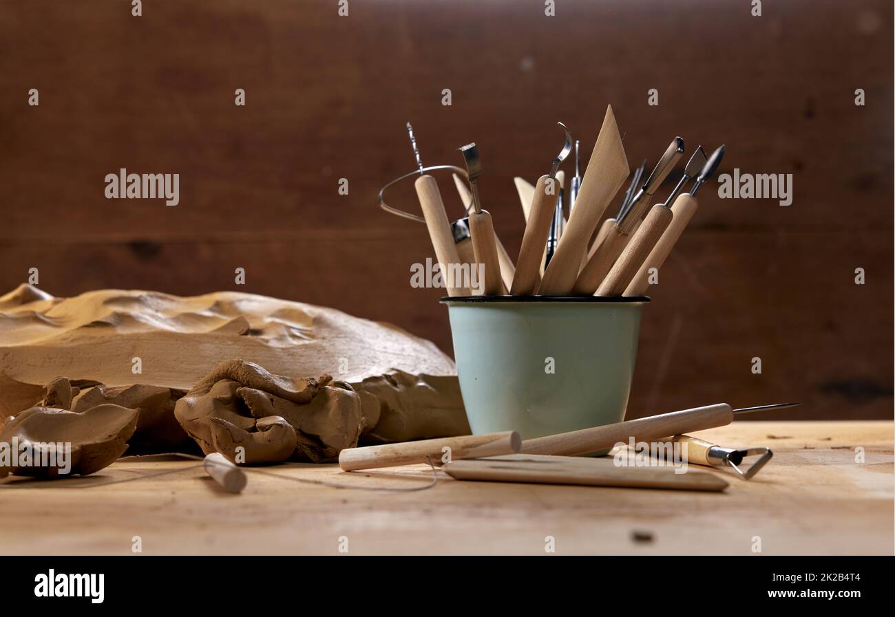Abundance of assorted special wooden tools for sculpting pottery in metal mug placed on table with clay in professional light workshop Stock Photo
