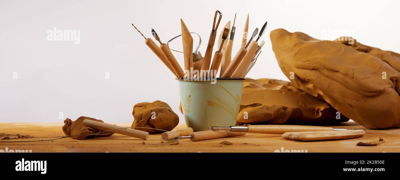 Set of professional instruments with wooden handles placed in mug on table with clay against white background in light workshop Stock Photo