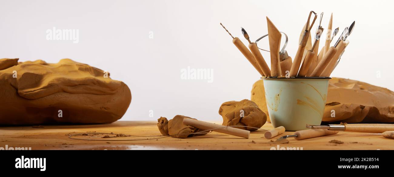 Heap of different tools for modeling pottery placed on table with clay against white background in light workshop Stock Photo