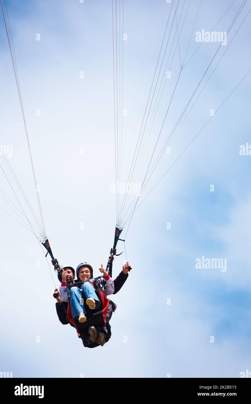 Thumbs up for paragliding. Low angle shot of two people tandem paragliding and giving a thumbs up. Stock Photo