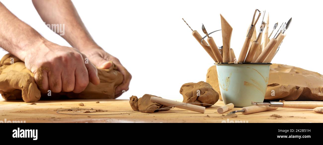 Crop anonymous master molding clay while making pottery on wooden table with various instruments against white background in light workshop Stock Photo