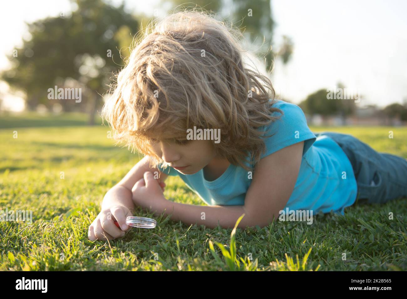 Summer kids outdoor portrait. Happy child with magnifying glass lying in grass. Environmental, ecology and environment concept. Stock Photo
