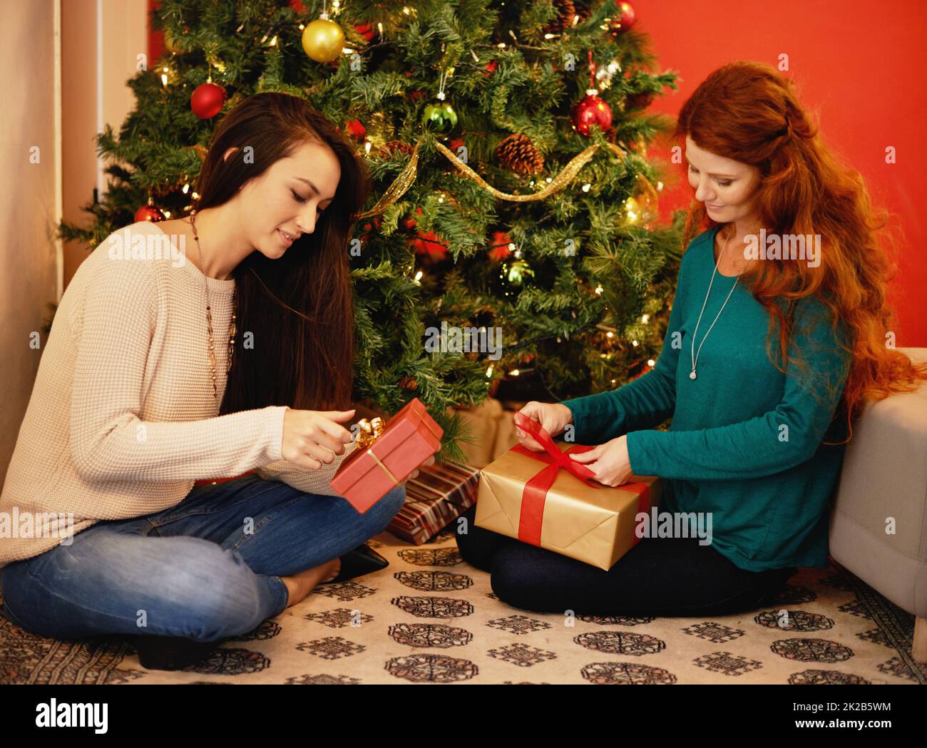 Theyre starting on the presents. two young women sitting by a christmas tree and opening their presents. Stock Photo