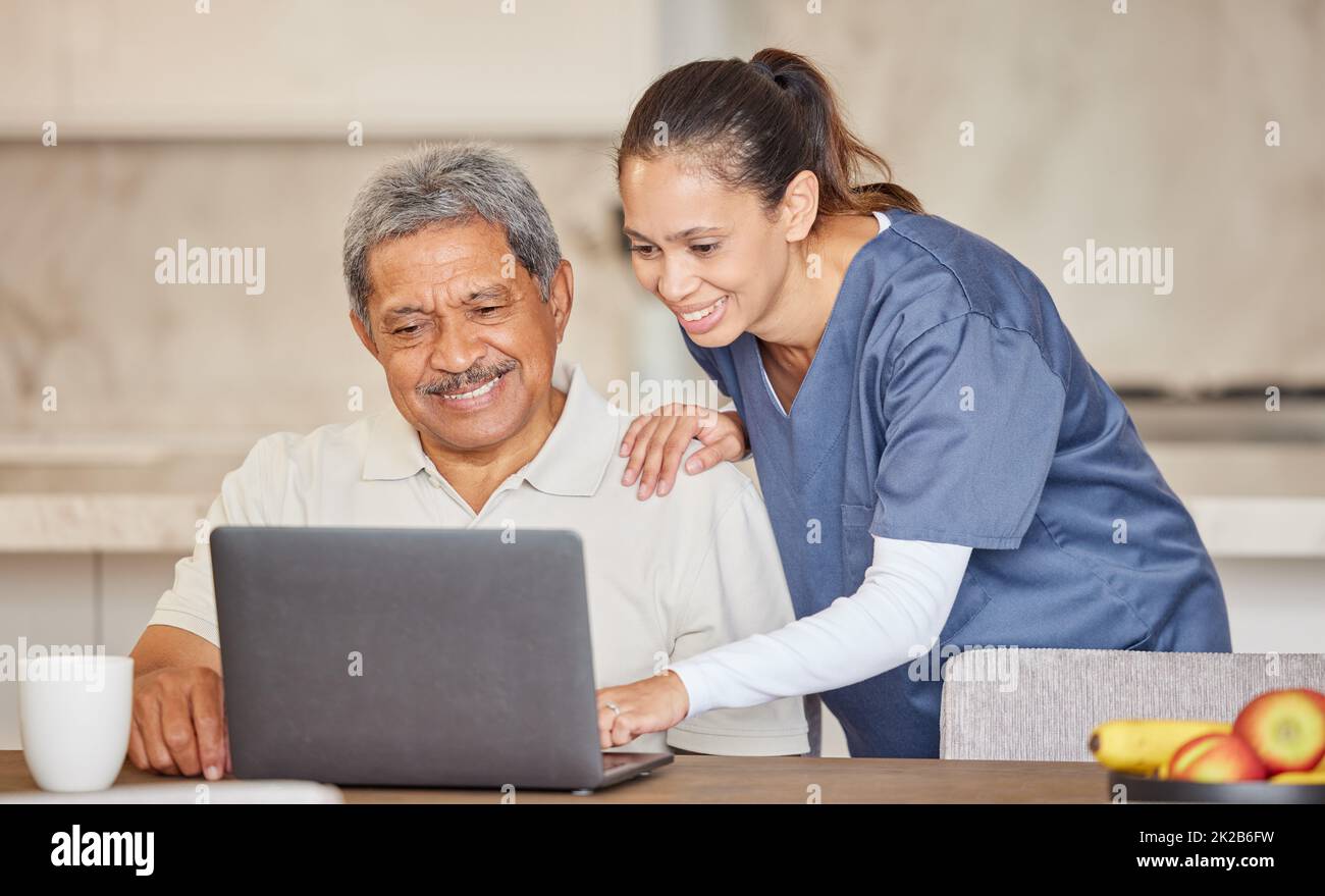 Happy nurse help senior man with laptop, showing how to make a video call or search the internet in an assisted living home. Senior patient enjoying Stock Photo