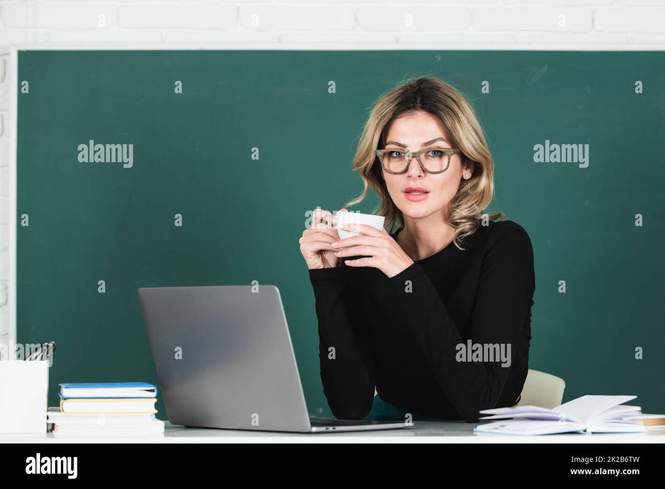 Portrait of female teacher teaching drinking coffee in classroom on blackboard. Stock Photo