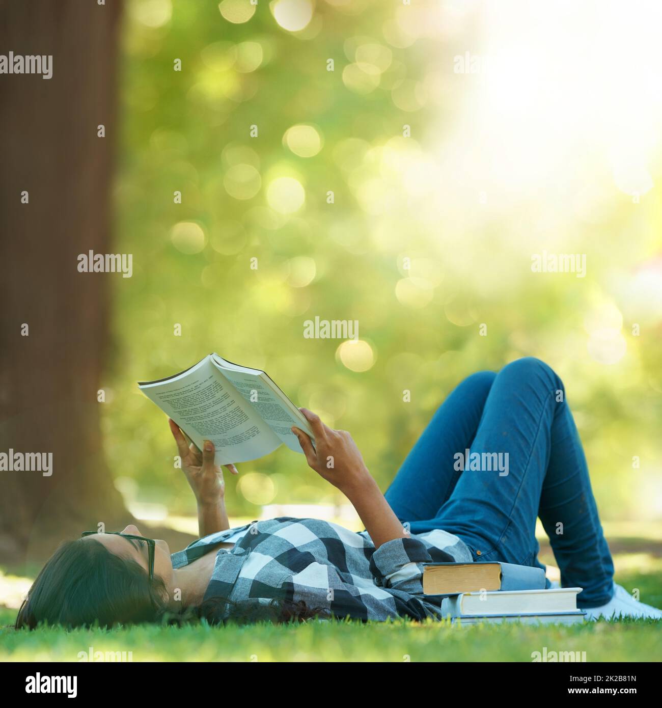 Lazy summer days. Shot of a young woman lying on grass and reading a book. Stock Photo